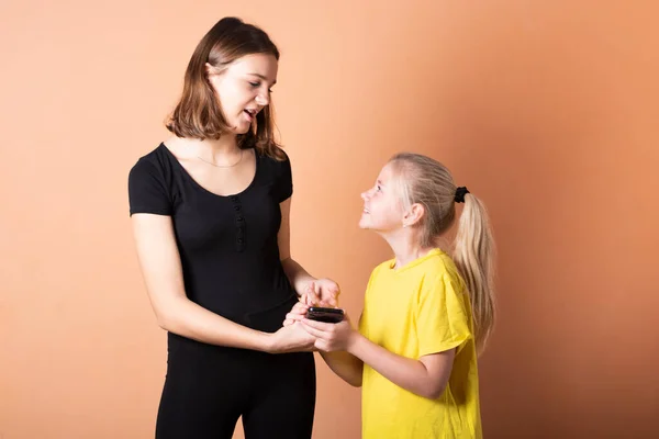 Sister asks her sister for a smartphone. on a light orange background.