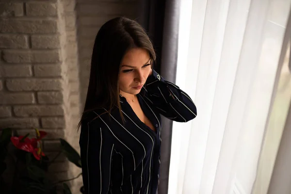 En vacker flicka, i svart skjorta, står nära fönstret. — Stockfoto