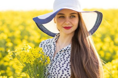 Kolza tarlasında, şapkalı, elinde bir buket kolza buketi olan bir kız. Yüksek kalite fotoğraf