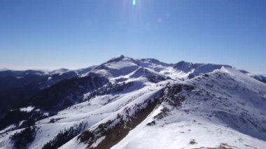 Panorama yatay. Birçok kişi, kayak beldesinde iyi bakımlı bir kayak pistine kayak yapmaya başlar. Güneş parlıyor ve gökyüzü parlak ve açık