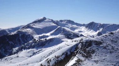 Panorama yatay. Birçok kişi, kayak beldesinde iyi bakımlı bir kayak pistine kayak yapmaya başlar. Güneş parlıyor ve gökyüzü parlak ve açık