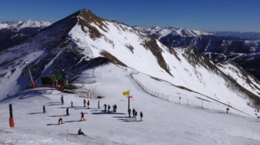 Panorama yatay. Birçok kişi, kayak beldesinde iyi bakımlı bir kayak pistine kayak yapmaya başlar. Güneş parlıyor ve gökyüzü parlak ve açık