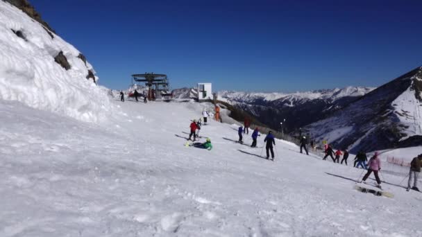 Панорама горизонтальная. Многие начинают кататься на лыжах на ухоженном горнолыжном курорте. Солнце светит, а небо ясное и ясное — стоковое видео