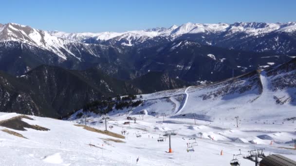 Панорама по горизонталі. Багато людей починають кататися на лижах на доглянутому гірськолижному схилі на гірськолижному курорті. Світить сонце, і небо яскраве і ясне — стокове відео