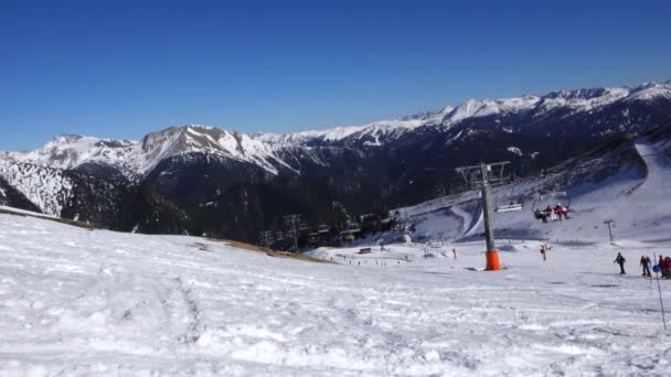 Panorama horizontal. Muitas pessoas começam a esquiar em uma pista de esqui bem preparada em uma estância de esqui. O sol está brilhando e o céu é claro e brilhante — Vídeo de Stock