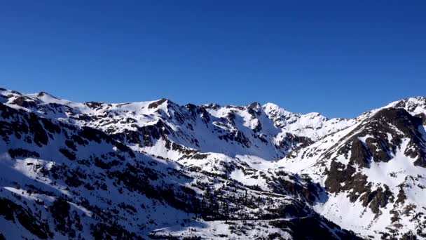 Πανόραμα οριζόντια. Πολλοί άνθρωποι ξεκινούν σκι σε μια καλά καλλωπισμένο πίστα σκι σε ένα χιονοδρομικό θέρετρο. Ο ήλιος λάμπει και ο ουρανός είναι φωτεινός και καθαρός — Αρχείο Βίντεο