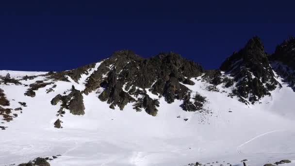 Πανόραμα οριζόντια. Πολλοί άνθρωποι ξεκινούν σκι σε μια καλά καλλωπισμένο πίστα σκι σε ένα χιονοδρομικό θέρετρο. Ο ήλιος λάμπει και ο ουρανός είναι φωτεινός και καθαρός — Αρχείο Βίντεο