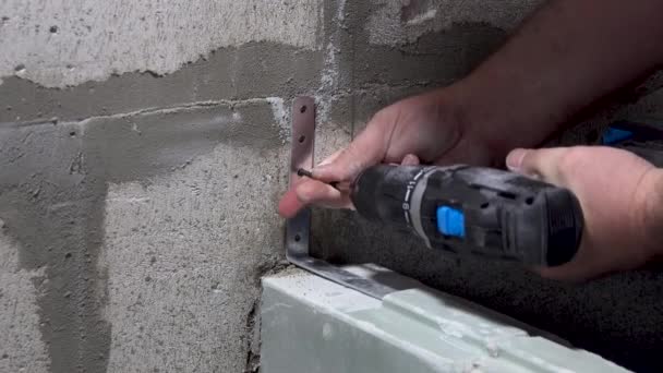 Munkás csavarok egy sarokban a falra egy csavarhúzóval — Stock videók