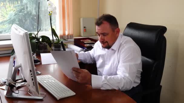 Young man the director of the company is sitting in the office looking at documents — Stock Video