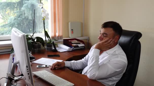 De jonge man de directeur van het bedrijf zit in het kantoor en werkt, maar hij valt in slaap op de werkplek — Stockvideo