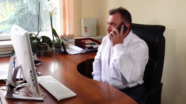 Νεαρέ, ο διευθυντής της εταιρείας κάθεται στο γραφείο και μιλάει συναισθηματικά στο τηλέφωνο. — Αρχείο Βίντεο