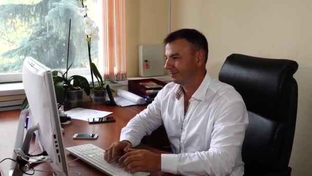El joven el director de la empresa se sienta en la oficina y emocionalmente trabaja, muy contento con su trabajo — Vídeos de Stock