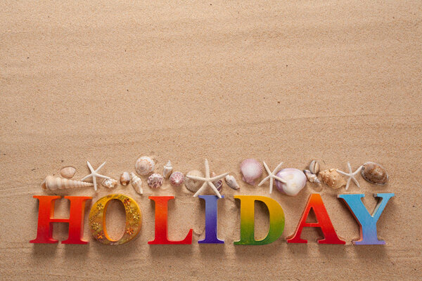 holiday written in colorful letters and seashell on the beach with copy space