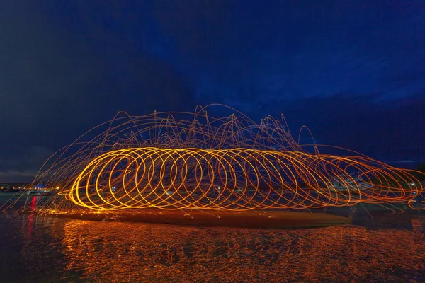 reflection of spark fire swirl from steel wool with long exposure speed motion abstract at sunrise in the sea