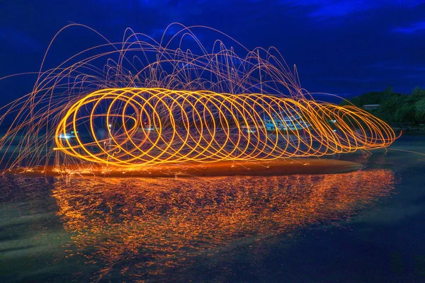 reflection of spark fire swirl from steel wool with long exposure speed motion abstract at sunrise in the sea