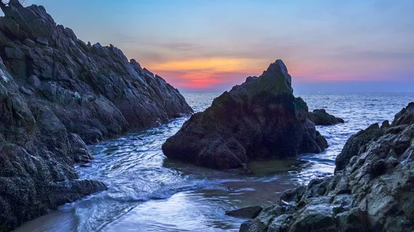 waves hit the big cone shape rock in the middle of stone cape during sunset at banana beach Phuket