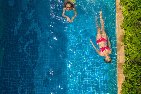 aerial top view above swimming pool. woman in yellow bikini and woman in red bikini are swimming