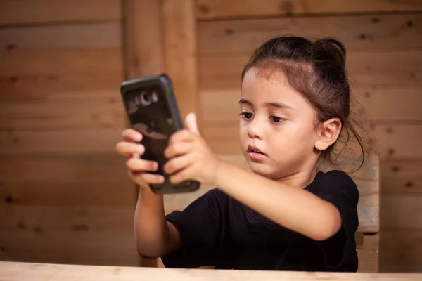 Bir Çocuk Giyim Siyah Tişört Ahşap Odada Cep Telefonunu Izliyor — Stok fotoğraf