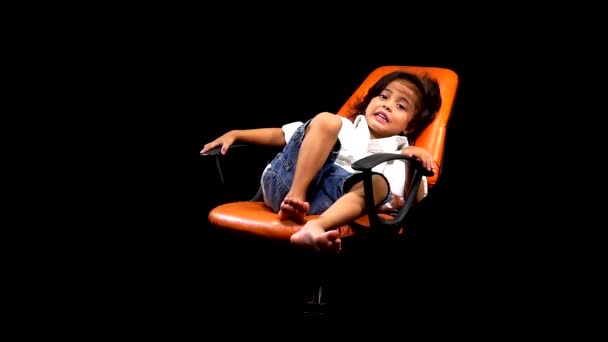 Zeitlupe Liegt Ein Kind Auf Einem Orangefarbenen Stuhl Vor Schwarzem — Stockvideo