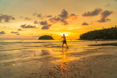 Turistler altın gün batımında plajda frizbi oynuyorlar Kata plajı Phuket Tayland 'da.