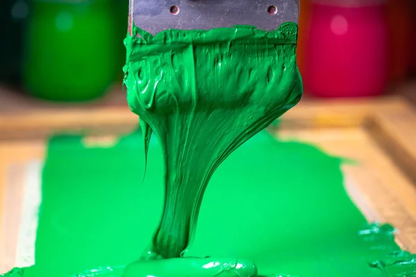 green color dripping from hand screen printing during printing tee shirt in tee shirt factory.