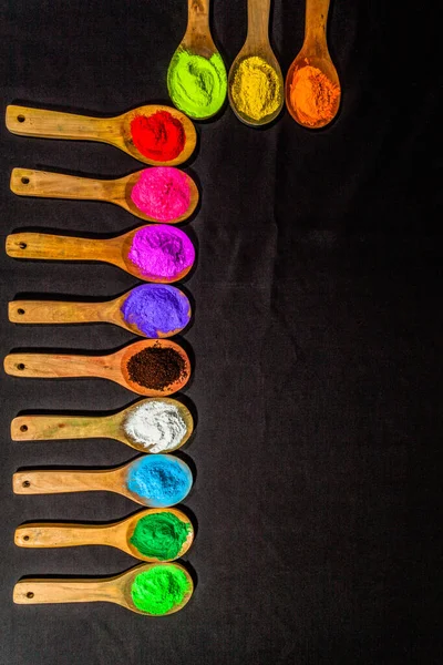 a row of colorful powder colors on wooden spoon in black background