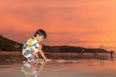 Gün batımında Phuket 'te, Kata plajında kum oynayan sevimli bir çocuk..