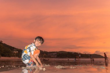 Gün batımında Phuket 'te, Kata plajında kum oynayan sevimli bir çocuk..