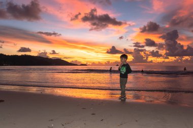 Gün batımında Patong sahilinde duran sevimli bir çocuk.