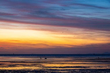 Gökyüzünde renkli bulutların harmanlandığı canlı bir gün batımının büyüleyici bir görüntüsü. Yüzücülerin siluetleri suyun tadını çıkarıyor. Anın güzelliği nefesini keser.