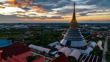Hava Wat Ketmadi Sriwararam perspektifi bulutlu mavi gökyüzü altında şehir ve kırsal alanlarla çevrili büyüleyici bir Tayland tapınak kompleksi sergiliyor..