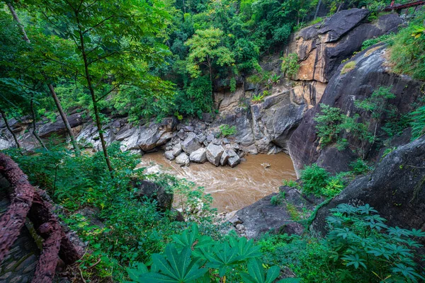 Yükselen kaya oluşumları ve uçurumları birbirine bağlayan dar bir köprüyle, yemyeşil ormanlarla çevrili bir nehir vadisinin pitoresk görüntüsü. Doğal güzellik ve canlı yeşillik. Öpücük uçurumu