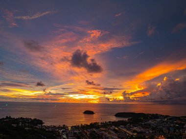 Nefes kesen bir günbatımı, kıyı kasabasının üzerinde turuncu ve mavi renkli canlı renkler çiziyor. Sahneyi çevreleyen yemyeşil tepeler var. Uzak bir tepe yapısı huzur dolu bir manzara ekler..  