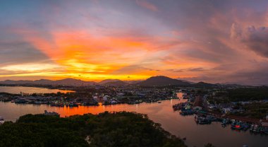 Phuket 'teki balıkçı limanında sersemletici gün batımını gösteren hava manzarası. Yumuşak mor renkten ateşli turuncu renklere dönüşen canlı gökyüzü, sakin ve pitoresk bir atmosfer yaratır..  