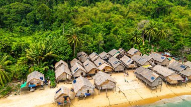 Phang Nga, Tayland-Mart, 20.2025: Yeşillik yeşil ormanlarla çevrili kıyı şeridi boyunca sıralanmış küçük kulübeleriyle tropikal bir sahil Morgan köyünün çarpıcı hava manzarası. Balıkçı tekneleri demirli.