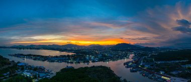 Phuket 'teki balıkçı limanında sersemletici gün batımını gösteren hava manzarası. Yumuşak mor renkten ateşli turuncu renklere dönüşen canlı gökyüzü, sakin ve pitoresk bir atmosfer yaratır..  