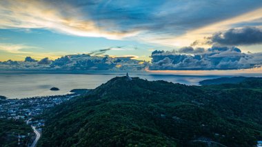 Nefes kesen bir gün batımının hava hiper yanılma görüntüsü sahneyi çevreleyen yemyeşil tepelerle dolu kıyı kasabasının üzerinde turuncu ve mavi renkli gökyüzünü resmediyor. Okyanusun üzerinde dramatik gün batımı bulutu