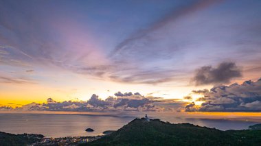 Nefes kesen bir gün batımının hava hiper yanılma görüntüsü sahneyi çevreleyen yemyeşil tepelerle dolu kıyı kasabasının üzerinde turuncu ve mavi renkli gökyüzünü resmediyor. Okyanusun üzerinde dramatik gün batımı bulutu