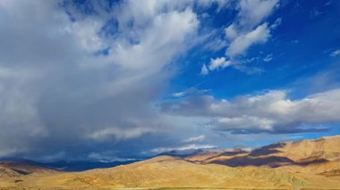 Huysuz bir bulutun altında zaman kaybı, nehir yatağındaki çatlaklarla işaretlenmiş uçsuz bucaksız yıpranmış. Ağaçlarla çevrili uzak tepeler görüntüye derinlik katıyor. Atmosfer hem sakin hem de evcilleştirilmemiş hissettiriyor.