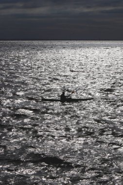 Adam bir kayık güneş parlamayı su yansıması Körfezi boyunca devam.