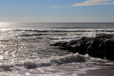 Rock ve kıyı üzerinde güneş ışığı ile deniz manzarası.