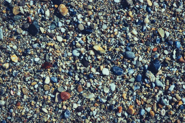 Muitas pedras pequenas molhadas na praia com pouca textura de seixos — Fotografia de Stock