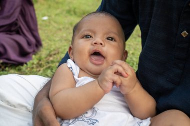 Bebek açık bir ağızla oturur, açık havada meraklı görünür.