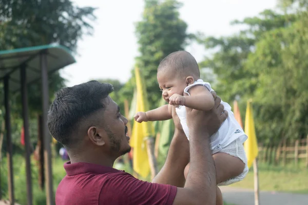 Bir ebeveyn bir bebeği kaldırıyor, yeşil bir ortamda neşeli bir an yaratıyor.