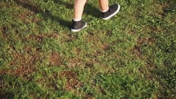 Un niño pequeño en pantalones cortos y zapatillas de deporte caminando sobre la hierba verde — Vídeos de Stock