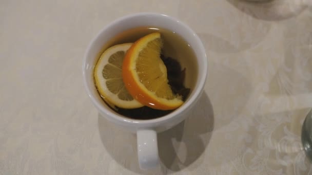 Чашка чая с ломтиками лимона и апельсина — стоковое видео