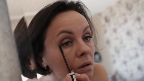 Eine nette Frau malt ihre Wimpern vor einem Spiegel. — Stockvideo