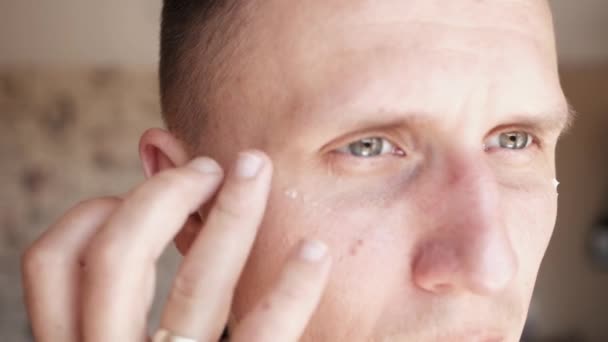 Witte metroseksuele man die lotion voor anti-aging behandeling rond het oog — Stockvideo