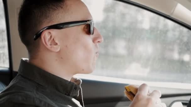 Muž jí hamburger za volantem automobilu. Nezdravé potraviny — Stock video