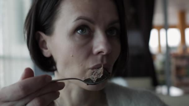 Linda garota morena comendo cheesecake e conversando com alguém em um café . — Vídeo de Stock